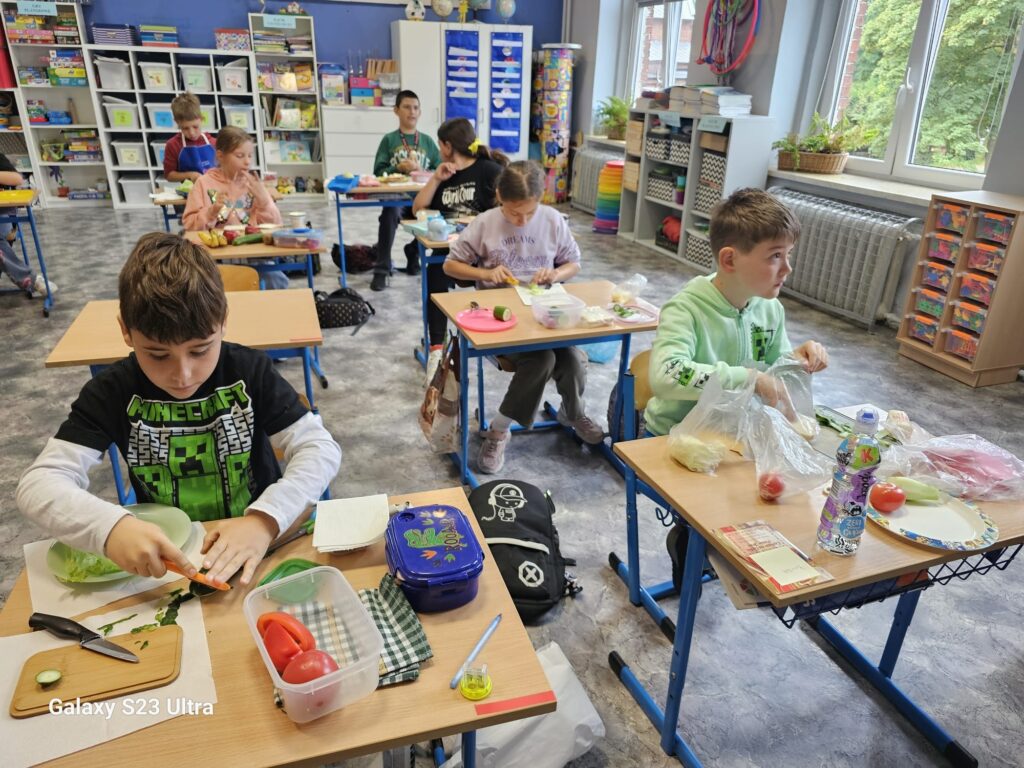 Uczniowie klasy 3 siedząc w swoich ławkach przygotowują zdrowe kanapki.