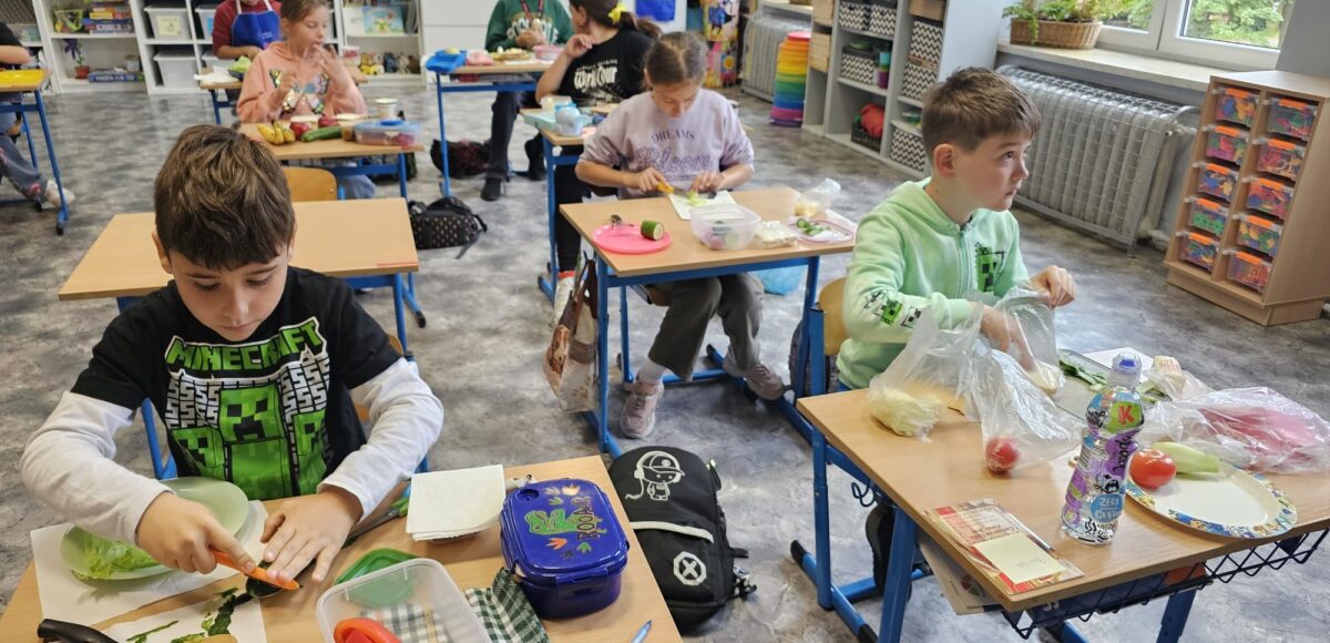 Uczniowie klasy 3 siedząc w swoich ławkach przygotowują zdrowe kanapki.