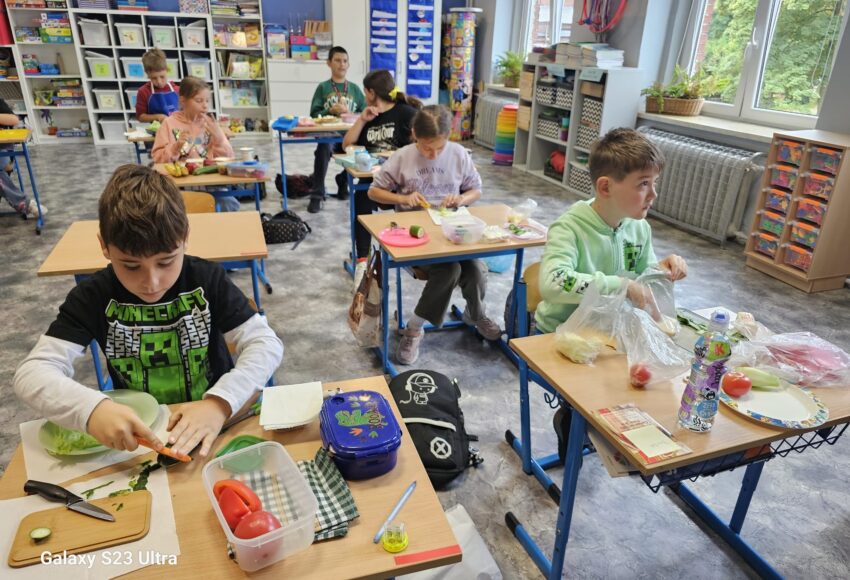 Uczniowie klasy 3 siedząc w swoich ławkach przygotowują zdrowe kanapki.