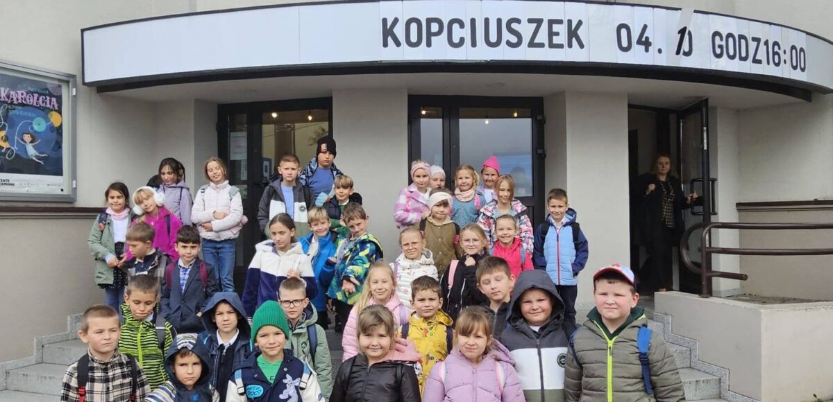 Grupa uczniów klas I–III stojąca przed wejściem do Teatru Dormana w Będzinie podczas wyjścia z okazji Dnia Chłopaka; dzieci pozują do wspólnego zdjęcia na schodach przed budynkiem teatru.