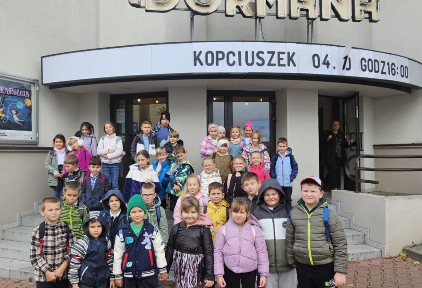 Grupa uczniów klas I–III stojąca przed wejściem do Teatru Dormana w Będzinie podczas wyjścia z okazji Dnia Chłopaka; dzieci pozują do wspólnego zdjęcia na schodach przed budynkiem teatru.