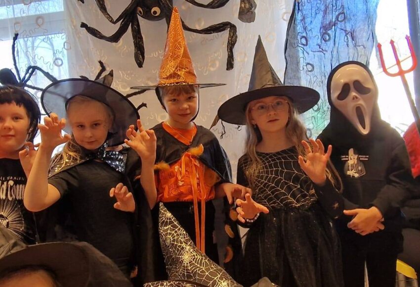 „Uczniowie w halloweenowych przebraniach podczas Upiornego Balu Halloweenowego w świetlicy szkolnej.”
