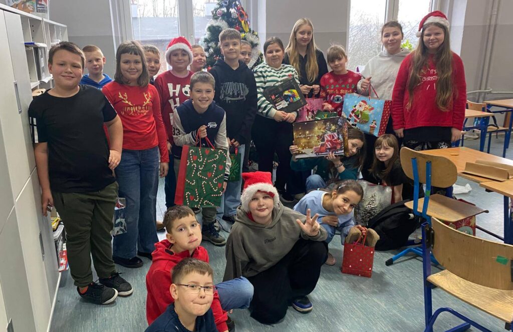 Grupa uczniów klasy 4a pozuje w sali lekcyjnej przy świątecznej choince, trzymając mikołajkowe upominki.