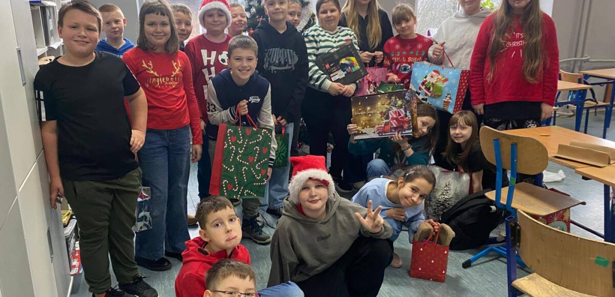 Grupa uczniów klasy 4a pozuje w sali lekcyjnej przy świątecznej choince, trzymając mikołajkowe upominki.