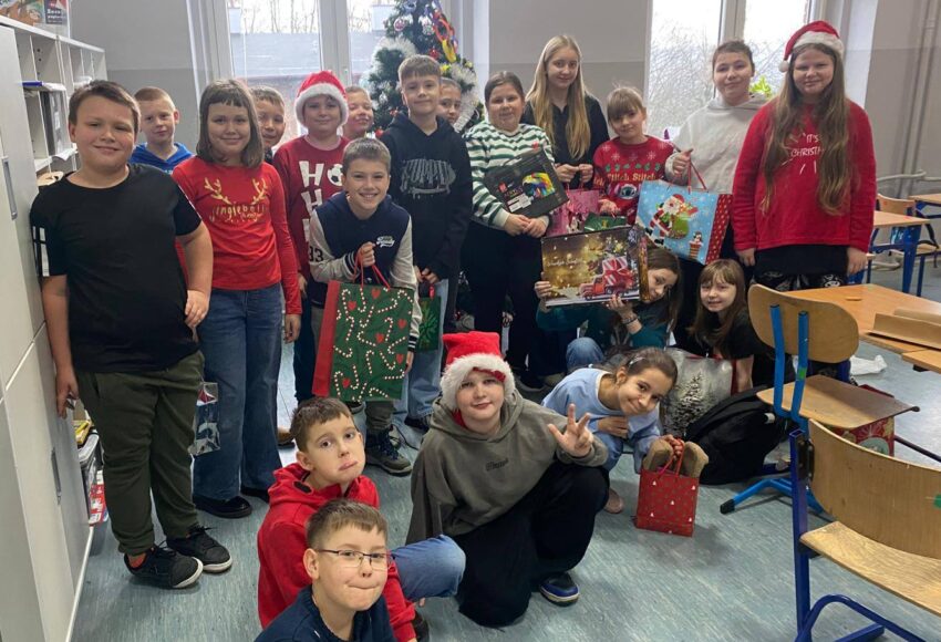 Grupa uczniów klasy 4a pozuje w sali lekcyjnej przy świątecznej choince, trzymając mikołajkowe upominki.