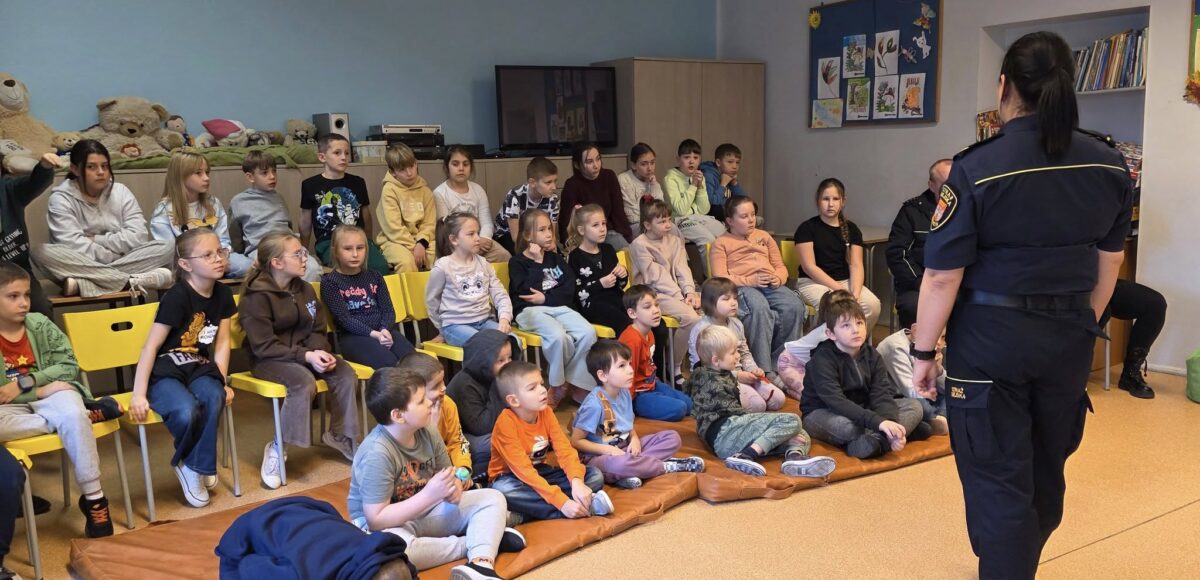 Na zdjęciu przedstawione są dzieci z klas 1-3 które słuchają Pani ze Straży Miejskiej, która prowadzi dla nich zajęcia na temat bezpieczeństwa