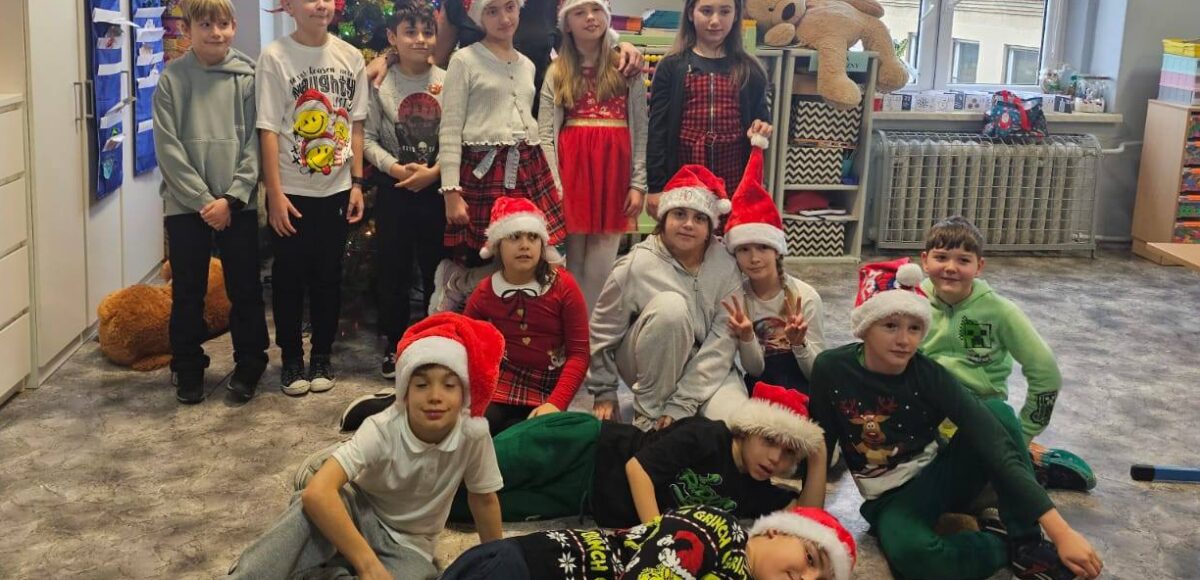 Zdjęcie przedstawia uczniów klasy 3 z wychowawczynią ubranych w czapki mikołajkowe na tle ubranej choinki