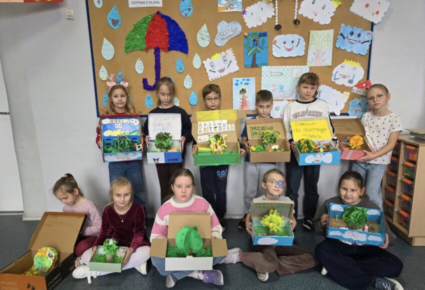 „Uczniowie klasy II prezentują wykonane prace plastyczno-techniczne związane z lekturą »Drzewo do samego nieba« w ramach projektu »Czytam z klasą – Lekturki spod chmurki«.”