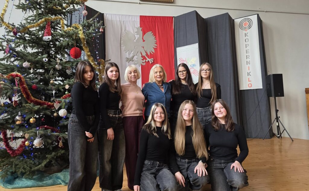 Zespół taneczny „Fantazja” wraz z opiekunką pozuje do zdjęcia na scenie I LO w Będzinie, obok udekorowanej świątecznej choinki i na tle godła oraz dekoracji wydarzenia.