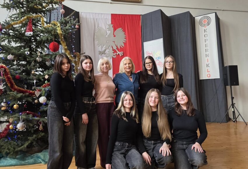 Zespół taneczny „Fantazja” wraz z opiekunką pozuje do zdjęcia na scenie I LO w Będzinie, obok udekorowanej świątecznej choinki i na tle godła oraz dekoracji wydarzenia.