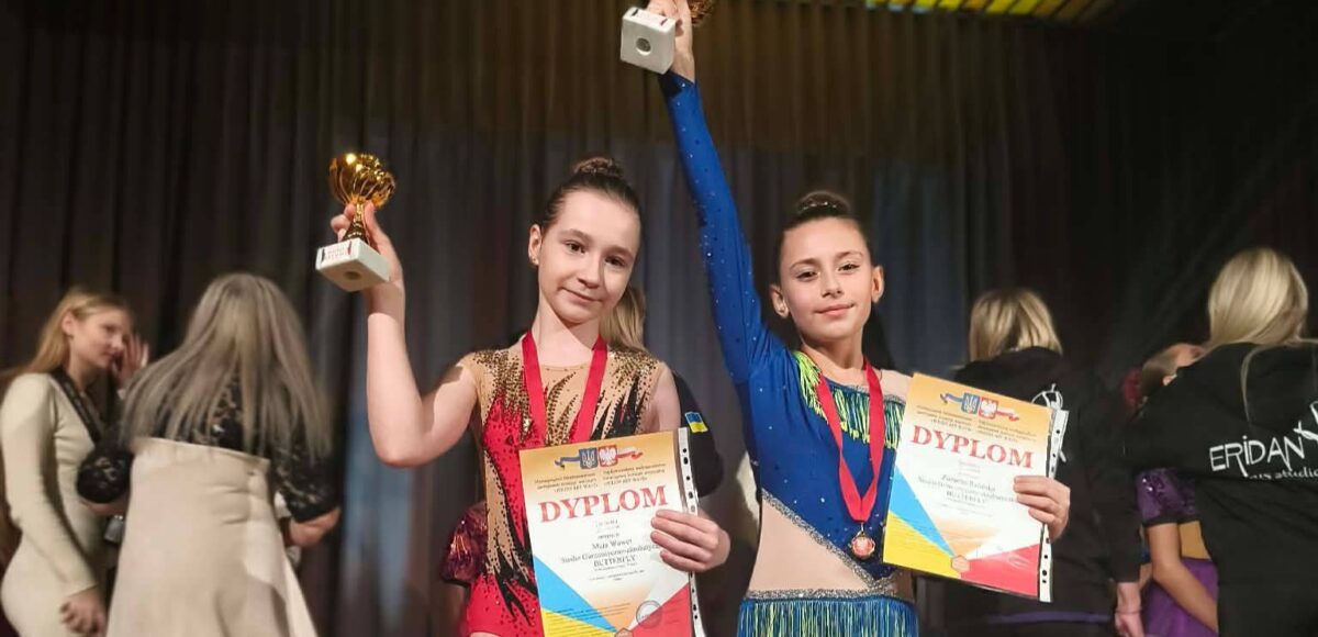 Uczennice Szkoły Podstawowej nr 6 prezentujące dyplomy i puchary podczas konkursu tanecznego „Polish Art Wave”. Dziewczęta stoją na scenie w strojach tanecznych i unoszą nagrody w górze.