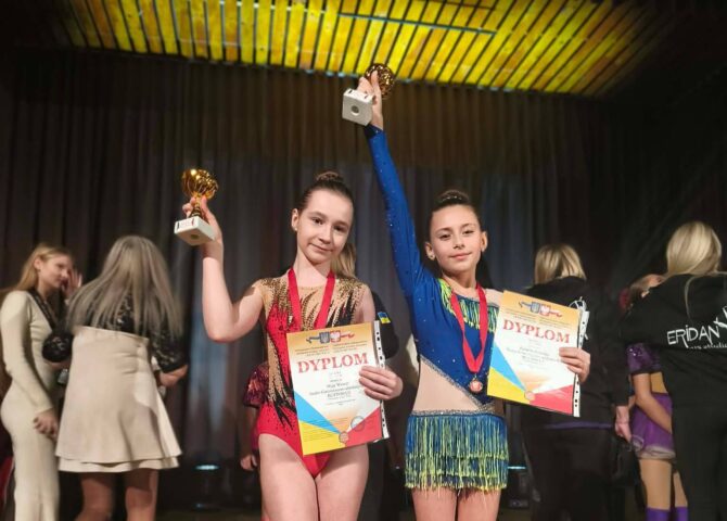 Uczennice Szkoły Podstawowej nr 6 prezentujące dyplomy i puchary podczas konkursu tanecznego „Polish Art Wave”. Dziewczęta stoją na scenie w strojach tanecznych i unoszą nagrody w górze.