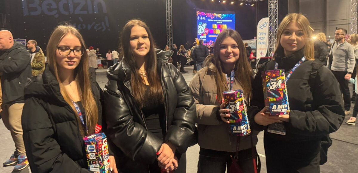 Szkolne wolontariuszki podczas 34. Finału Wielkiej Orkiestry Świątecznej Pomocy w hali Będzin Arena, trzymające puszki WOŚP na tle sceny wydarzenia.