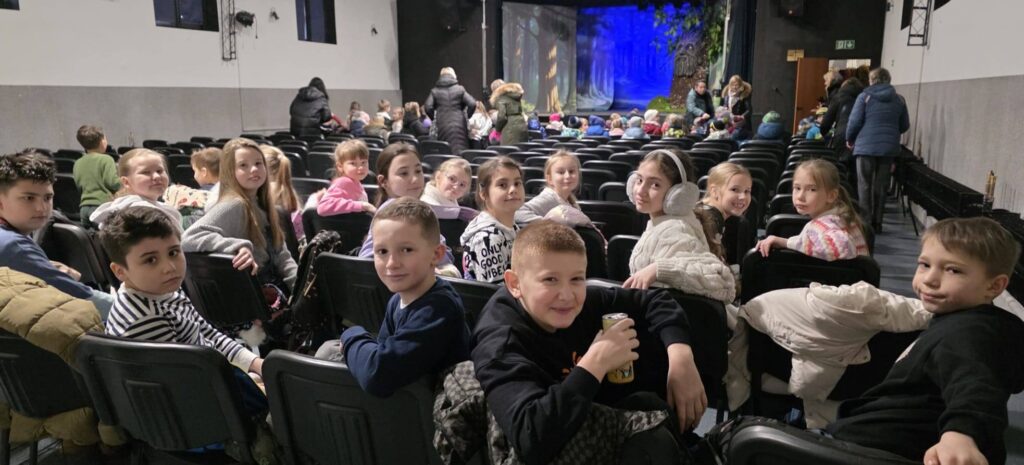 Uczniowie klas I–IV siedzą na widowni w Domu Kultury Grodziec przed rozpoczęciem musicalu »Pinokio«, oczekując na spektakl