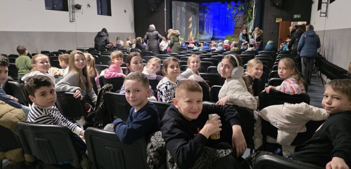 Uczniowie klas I–IV siedzą na widowni w Domu Kultury Grodziec przed rozpoczęciem musicalu »Pinokio«, oczekując na spektakl