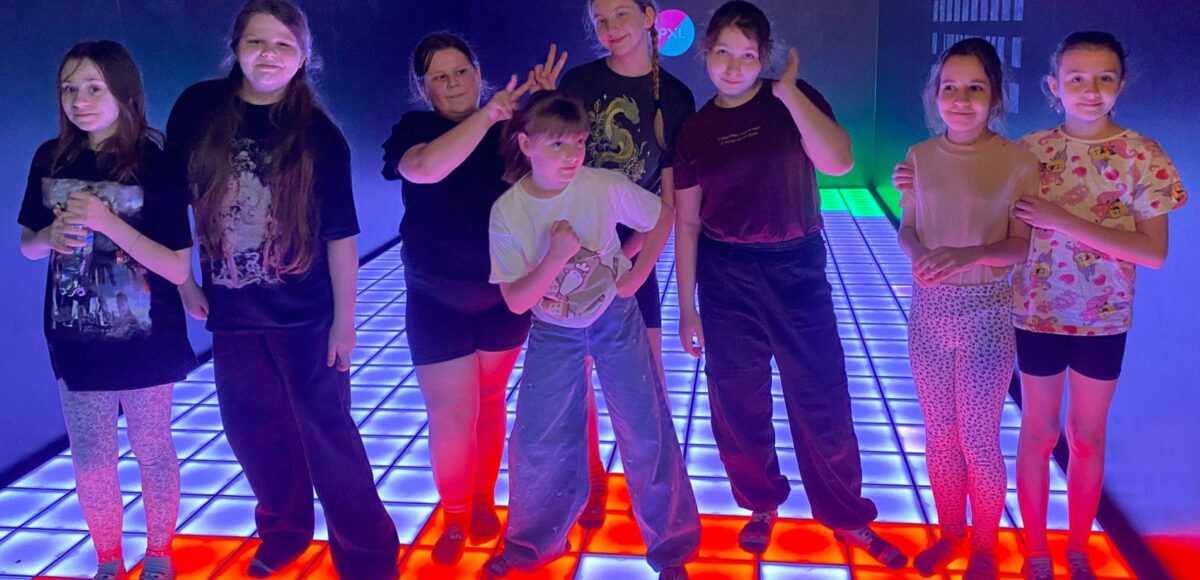 Grupa uczniów stojących na interaktywnej, podświetlanej podłodze w PixelXL w Katowicach podczas wspólnej zabawy integracyjnej.