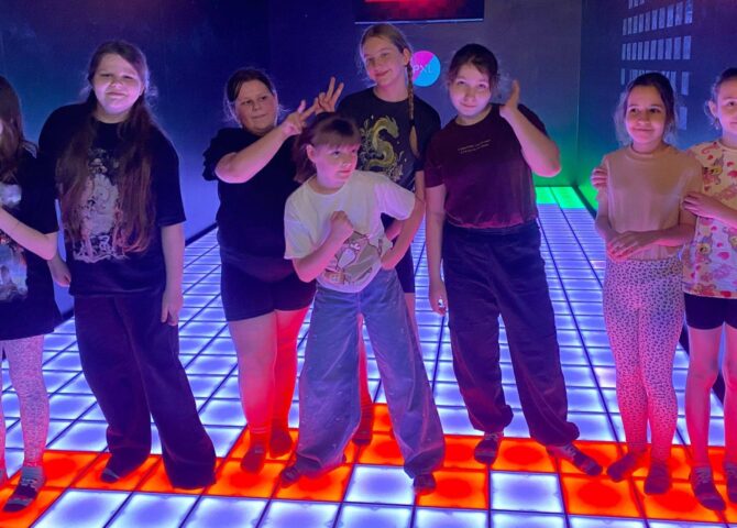 Grupa uczniów stojących na interaktywnej, podświetlanej podłodze w PixelXL w Katowicach podczas wspólnej zabawy integracyjnej.