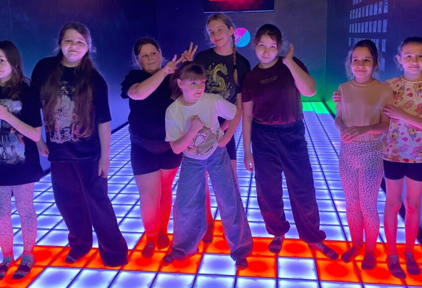 Grupa uczniów stojących na interaktywnej, podświetlanej podłodze w PixelXL w Katowicach podczas wspólnej zabawy integracyjnej.
