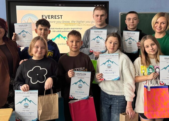 Uczniowie wraz z nauczycielami prezentują dyplomy i nagrody zdobyte w Ogólnopolskim Konkursie Języka Angielskiego EVEREST w szkolnej sali lekcyjnej.
