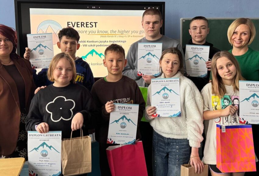 Uczniowie wraz z nauczycielami prezentują dyplomy i nagrody zdobyte w Ogólnopolskim Konkursie Języka Angielskiego EVEREST w szkolnej sali lekcyjnej.