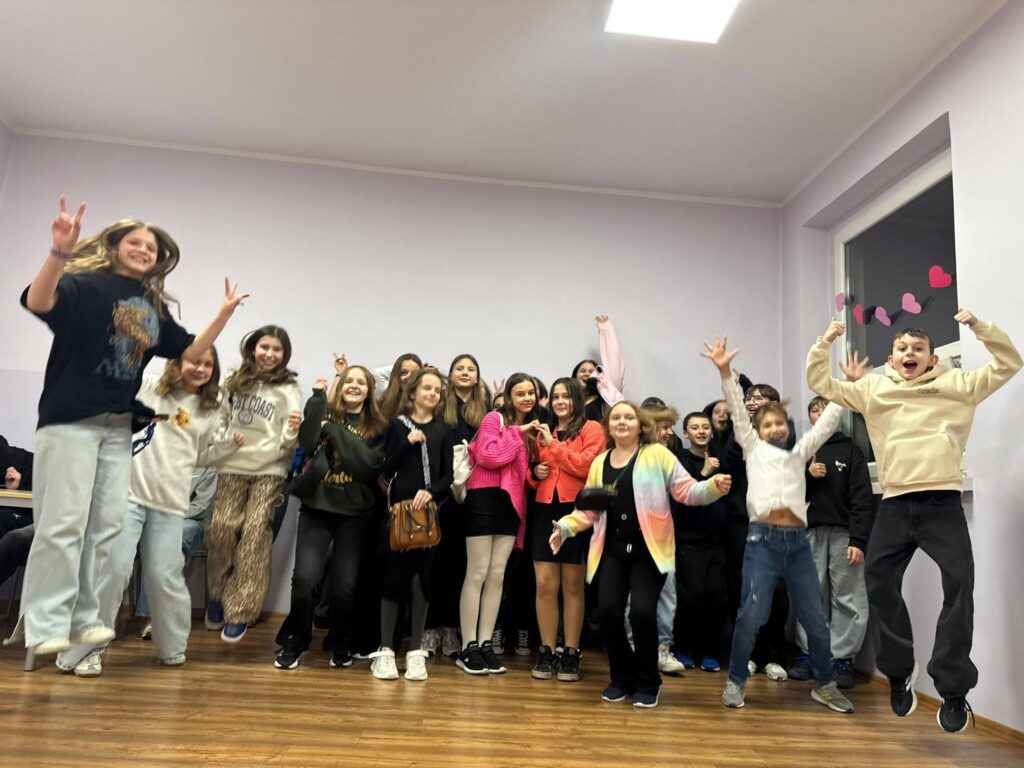 Uczniowie podczas dyskoteki karnawałowo-walentynkowej w szkolnej sali – grupa dzieci tańczy i skacze, pozując do wspólnego zdjęcia.”