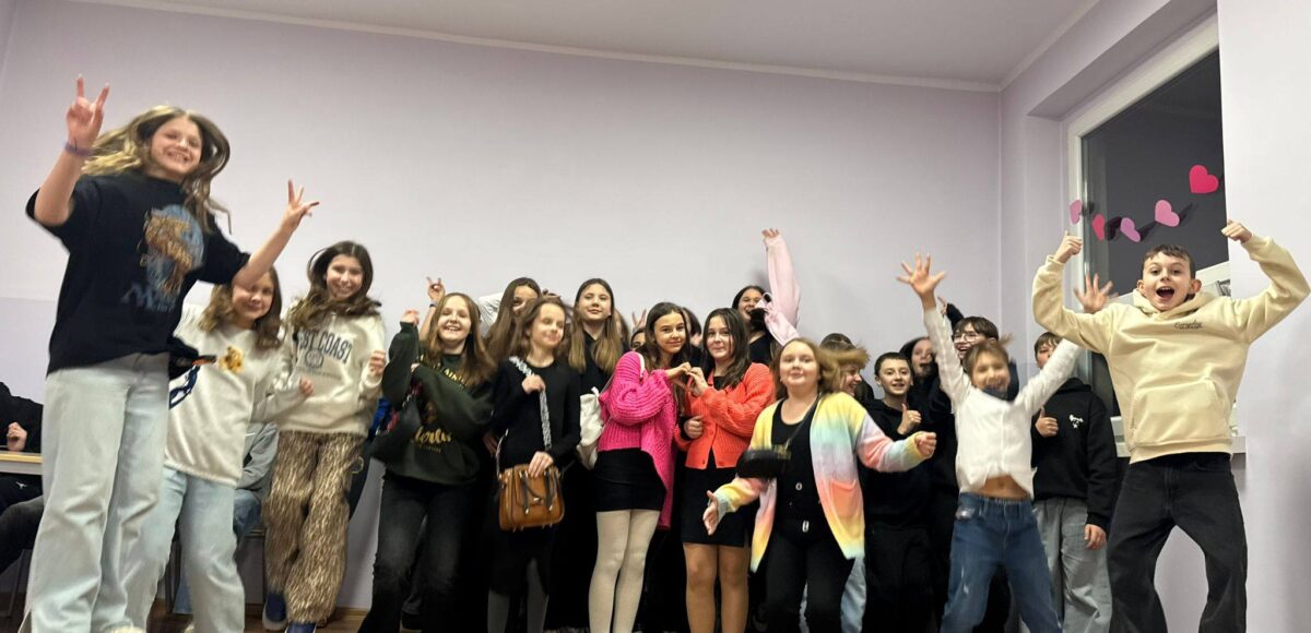 Uczniowie podczas dyskoteki karnawałowo-walentynkowej w szkolnej sali – grupa dzieci tańczy i skacze, pozując do wspólnego zdjęcia.”