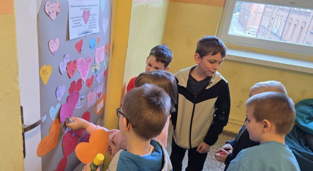 Uczniowie umieszczają kolorowe serca z tytułami ulubionych książek na tablicy w ramach akcji »Walentynki z książką« organizowanej przez Bibliotekę Szkolną.