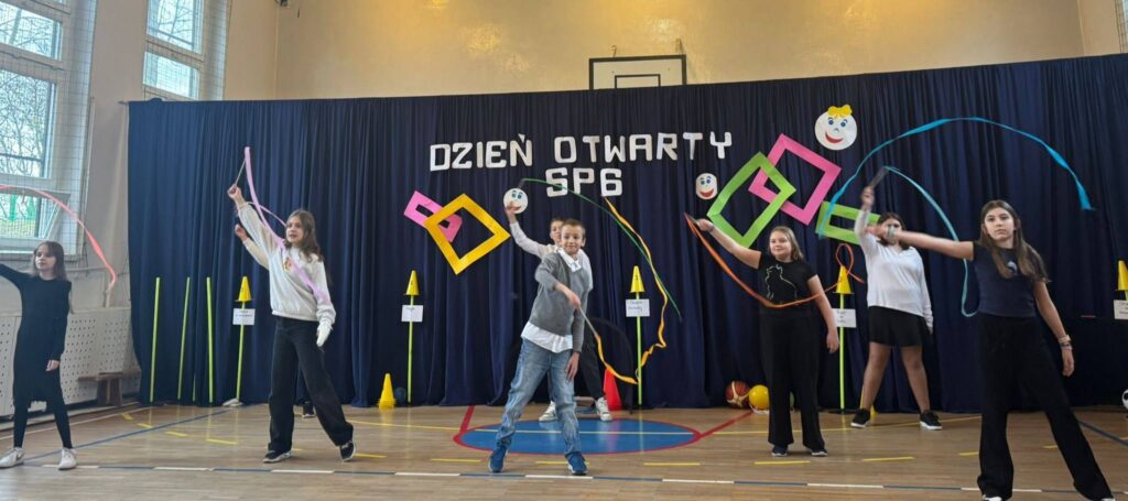 Uczniowie Szkoły Podstawowej nr 6 występują podczas Dnia Otwartego, prezentując układ z wstążkami na sali gimnastycznej.