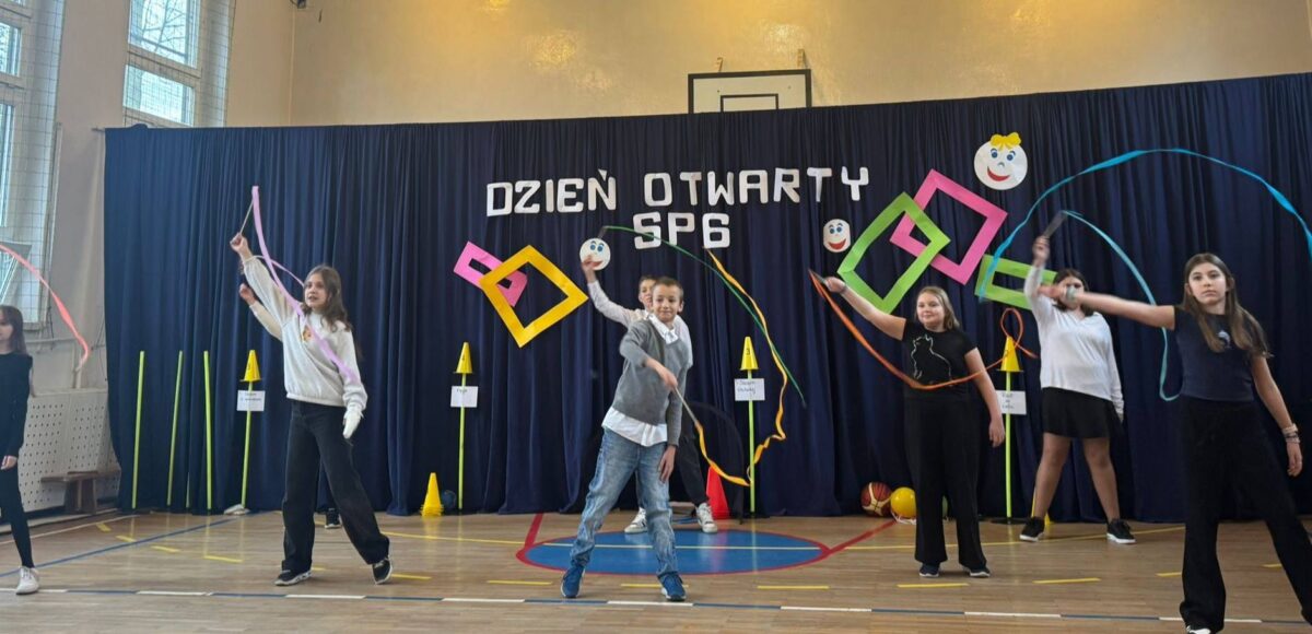 Uczniowie Szkoły Podstawowej nr 6 występują podczas Dnia Otwartego, prezentując układ z wstążkami na sali gimnastycznej.