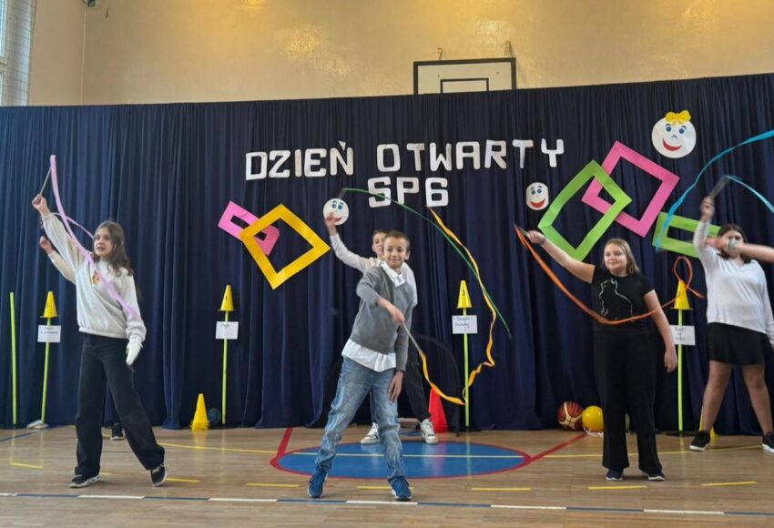 Uczniowie Szkoły Podstawowej nr 6 występują podczas Dnia Otwartego, prezentując układ z wstążkami na sali gimnastycznej.