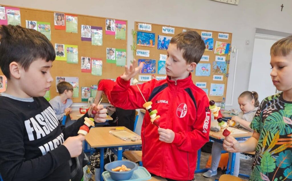 Uczniowie klasy 3 przygotowują owocowe szaszłyki podczas obchodów pierwszego dnia wiosny w sali lekcyjnej.
