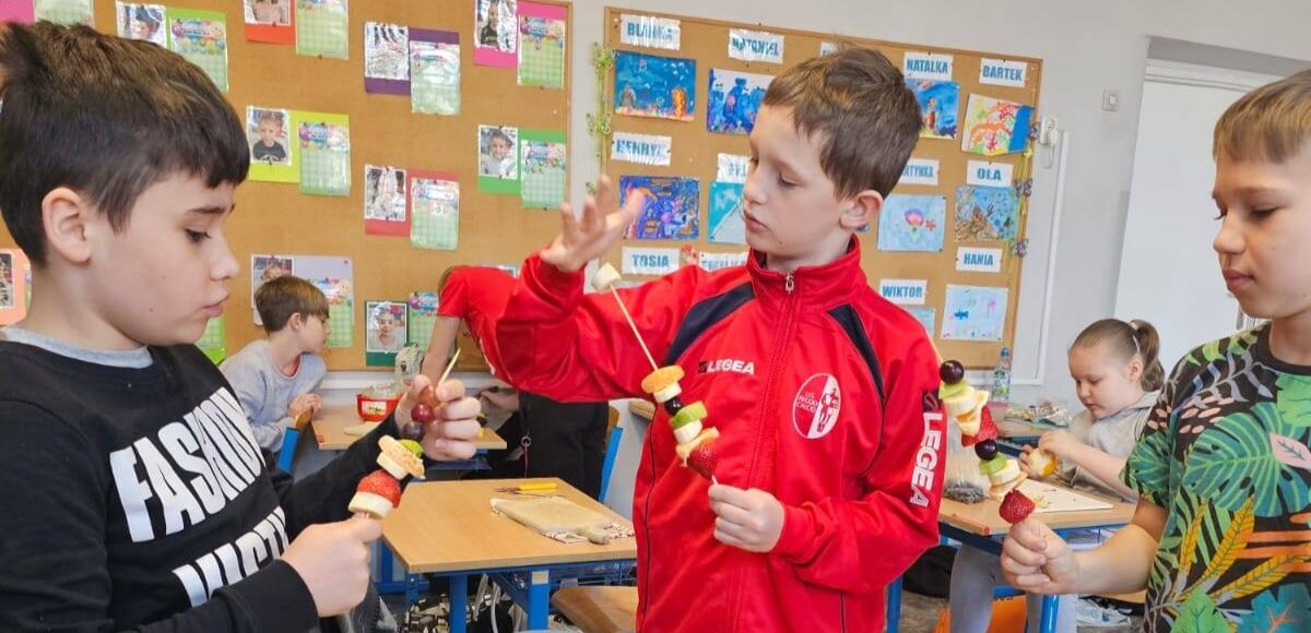 Uczniowie klasy 3 przygotowują owocowe szaszłyki podczas obchodów pierwszego dnia wiosny w sali lekcyjnej.