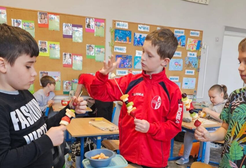 Uczniowie klasy 3 przygotowują owocowe szaszłyki podczas obchodów pierwszego dnia wiosny w sali lekcyjnej.