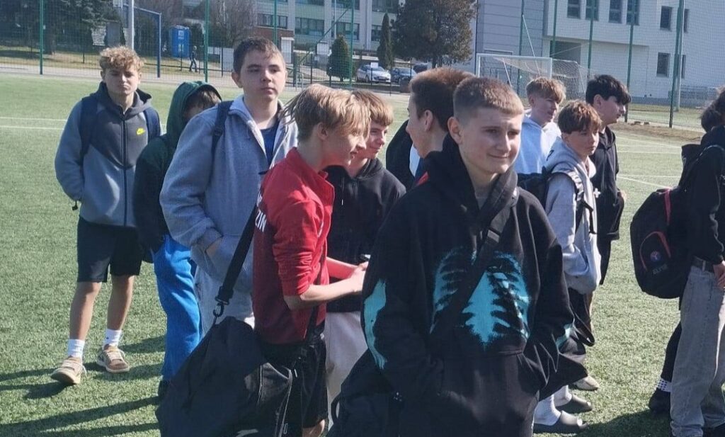 Uczniowie reprezentacji szkoły podczas miejskich zawodów piłki nożnej, stojący na boisku przed rozpoczęciem rozgrywek.
