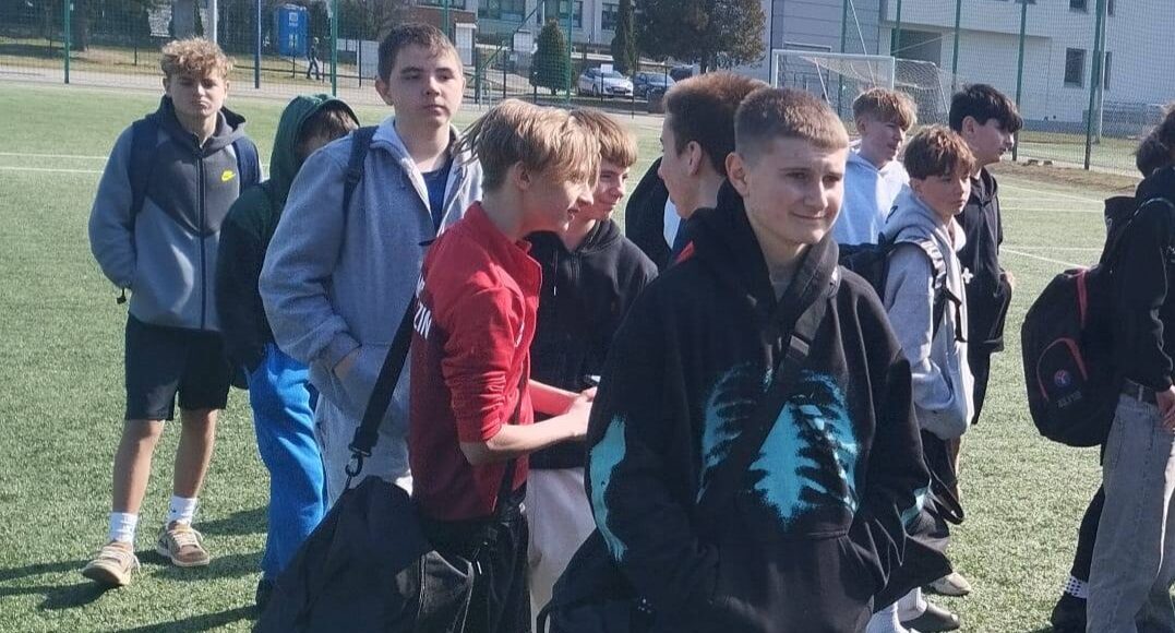 Uczniowie reprezentacji szkoły podczas miejskich zawodów piłki nożnej, stojący na boisku przed rozpoczęciem rozgrywek.