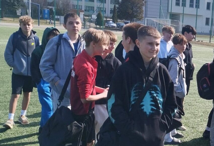 Uczniowie reprezentacji szkoły podczas miejskich zawodów piłki nożnej, stojący na boisku przed rozpoczęciem rozgrywek.
