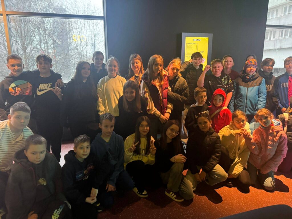 Uczniowie klas 5 i 6 pozują do wspólnego zdjęcia podczas wycieczki do Pixel XL w Katowicach, stojąc w nowoczesnej przestrzeni rozrywkowej