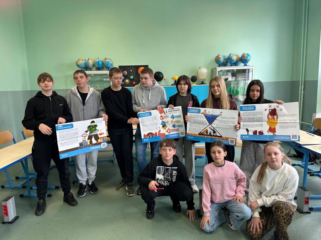 Uczniowie pozują w sali lekcyjnej, prezentując plansze edukacyjne dotyczące oszczędzania wody i globalnych problemów związanych z dostępem do wody w ramach Światowego Dnia Wody.