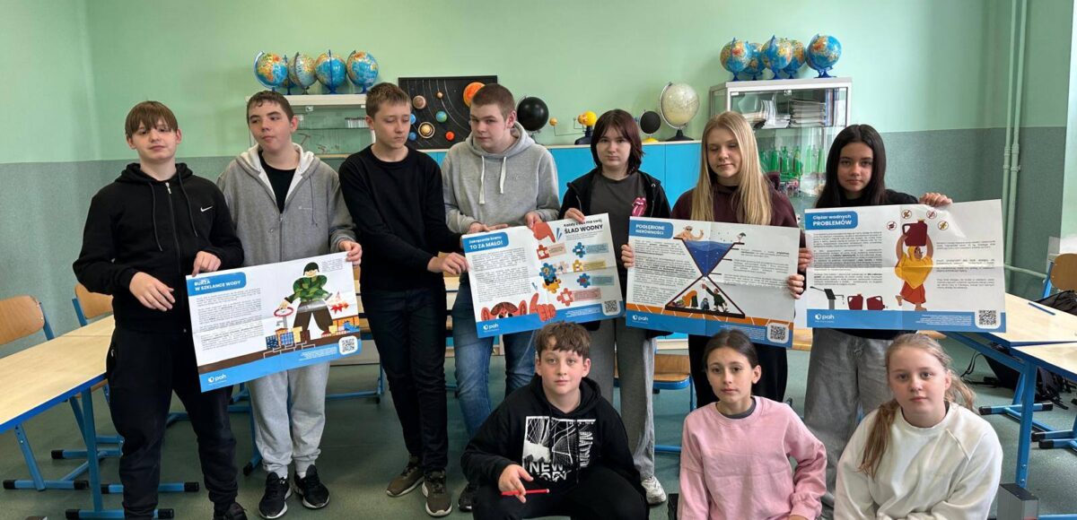 Uczniowie pozują w sali lekcyjnej, prezentując plansze edukacyjne dotyczące oszczędzania wody i globalnych problemów związanych z dostępem do wody w ramach Światowego Dnia Wody.