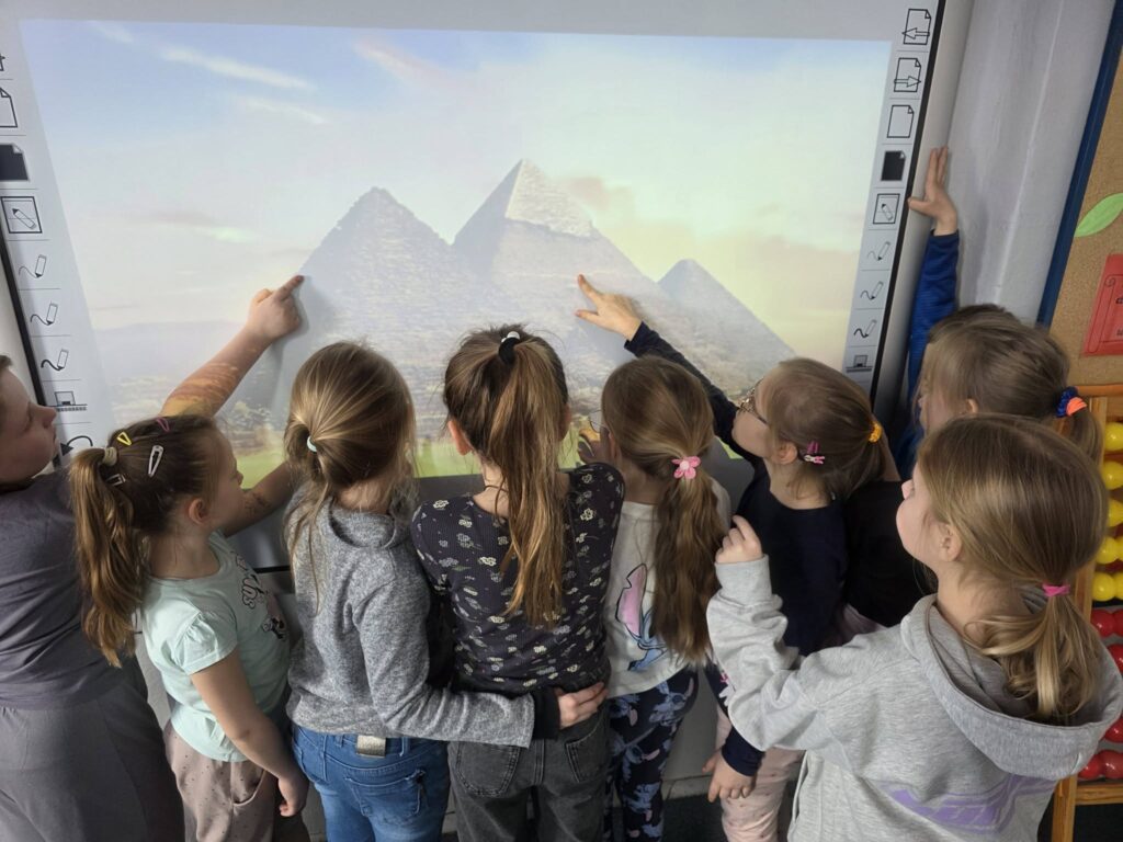 Uczniowie klas 2 podczas zajęć oglądają i wskazują na tablicy multimedialnej piramidy w Gizie, poznając sztukę i architekturę starożytnego Egiptu.