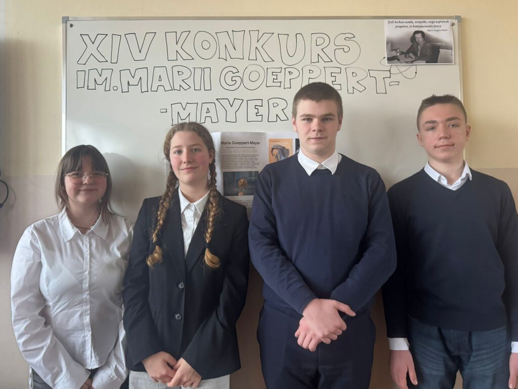Uczniowie szkoły pozujący na tle tablicy z napisem „XIV Konkurs im. Marii Goeppert-Mayer”, reprezentujący szkołę w konkursie interdyscyplinarnym w języku angielskim.