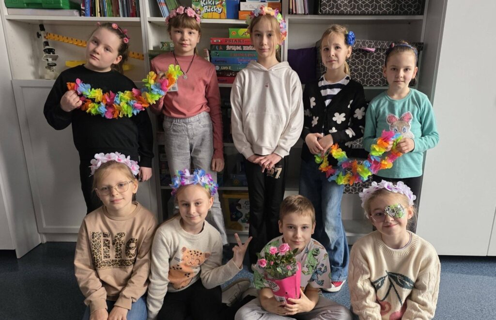 Uczniowie pozują w sali lekcyjnej, prezentując kolorowe kwiatowe opaski i girlandy, przygotowane w ramach wiosennego dnia „Kwiaty we włosach