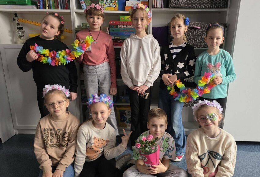 Uczniowie pozują w sali lekcyjnej, prezentując kolorowe kwiatowe opaski i girlandy, przygotowane w ramach wiosennego dnia „Kwiaty we włosach