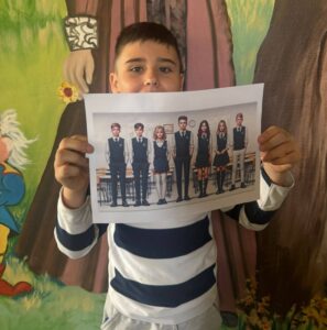 Uczeń prezentuje wizualizację szkolnych mundurków przygotowaną z okazji Prima Aprilis, trzymając wydruk przedstawiający uczniów w jednakowych strojach.