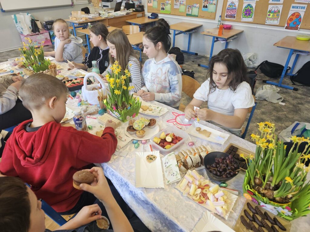 Uczniowie klasy 3 podczas wielkanocnego spotkania przy stole, dekorujący słodkości i wspólnie świętujący w klasie.