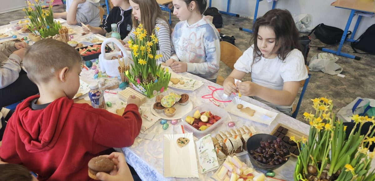 Uczniowie klasy 3 podczas wielkanocnego spotkania przy stole, dekorujący słodkości i wspólnie świętujący w klasie.