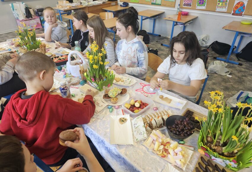 Uczniowie klasy 3 podczas wielkanocnego spotkania przy stole, dekorujący słodkości i wspólnie świętujący w klasie.