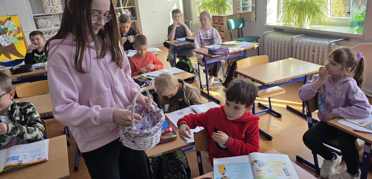 Uczniowie w klasie podczas obchodów Prima Aprilis losują „tajne kody” z koszyka, uczestnicząc w przygotowanej przez Samorząd Uczniowski zabawie.