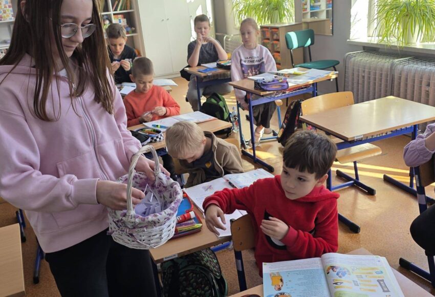 Uczniowie w klasie podczas obchodów Prima Aprilis losują „tajne kody” z koszyka, uczestnicząc w przygotowanej przez Samorząd Uczniowski zabawie.