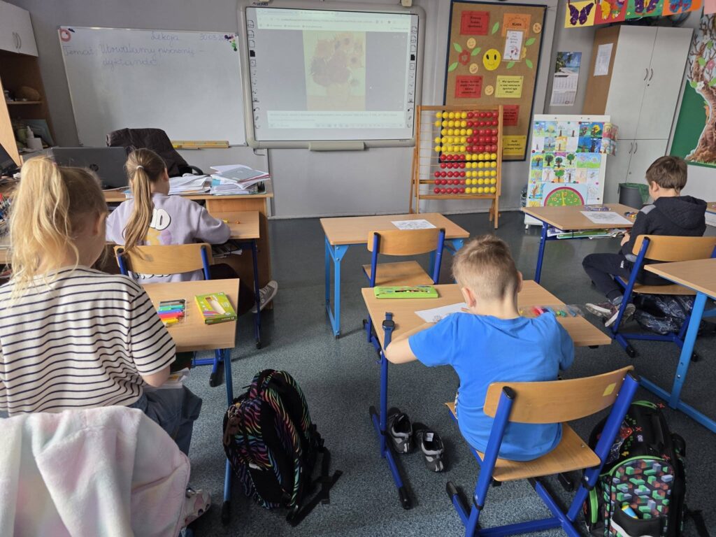 Uczniowie podczas zajęć plastycznych w klasie, pracują przy ławkach, inspirując się twórczością Vincenta van Gogha wyświetlaną na tablicy interaktywnej.